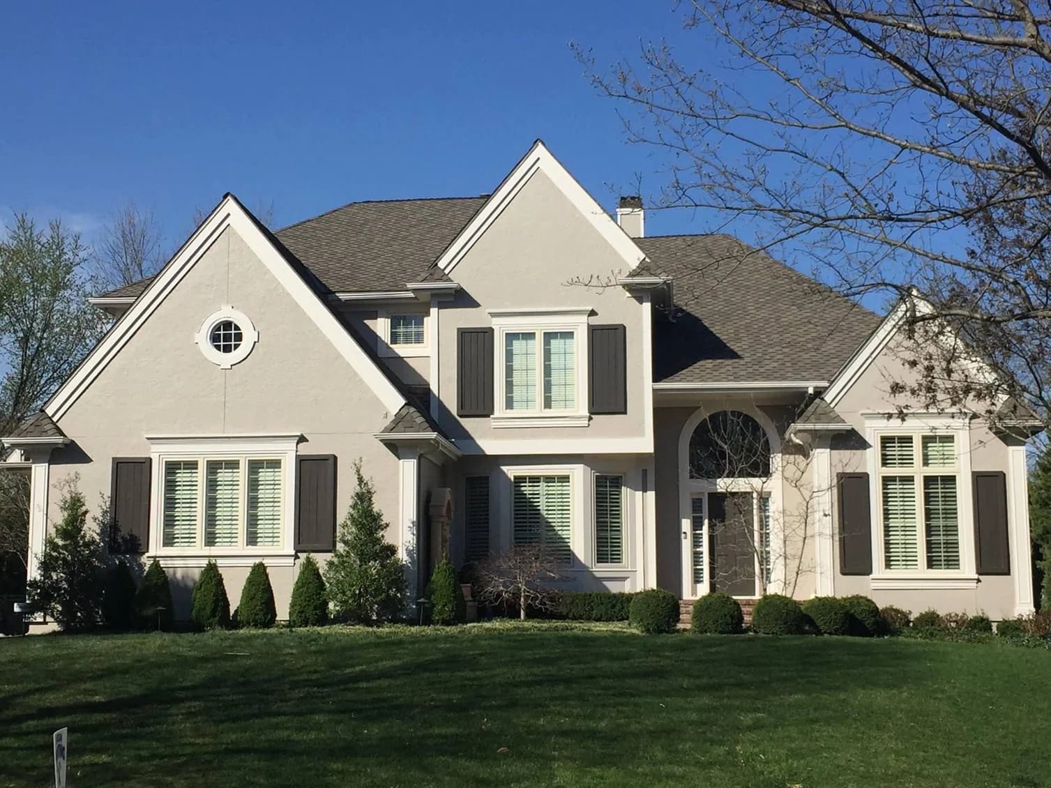 This is an image from Brogan Painting & Remodeling. The image shows a light-beige stucco home with freshly painted trim and shutters.