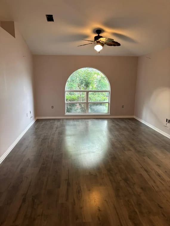 This is an image from HH Painting company, located in Gainesville, FL. The image is a freshly painted interior room with soft beige walls, dark wood vinyl flooring, and arched window with natural light
