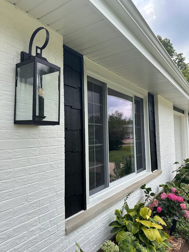 Exterior painting project by Allegiant Painting LLC in Lakemoor, Illinois. The image shows white brick, black shutters, white trim, and a wall lantern.