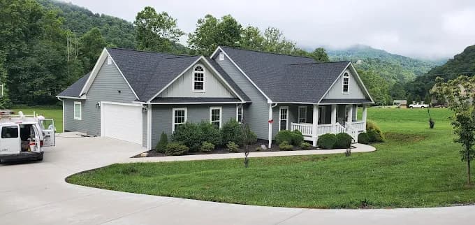 Exterior painting project by Huskey's Paint & Design in Sylva, NC. The image shows a gray home with white trim, dormer windows, a lawn, and mountain hills.