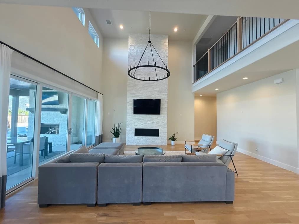 This is an image from Spray Tex Painting, located in Texas. The image displays a spacious living room with tall ceilings, a stone fireplace, a large sectional sofa, and expansive sliding glass doors.