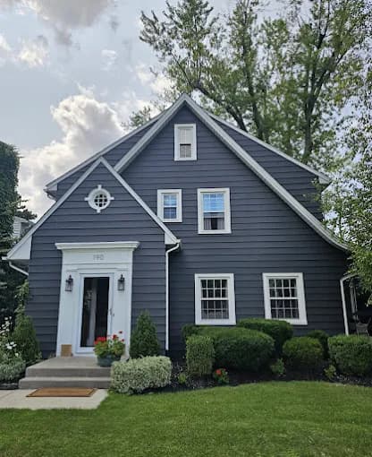 This is an image from BEE Pro Painting, located in New Jersey. The image shows a freshly painted dark gray residential home exterior with crisp white trim, updated siding, and well-maintained landscaping.