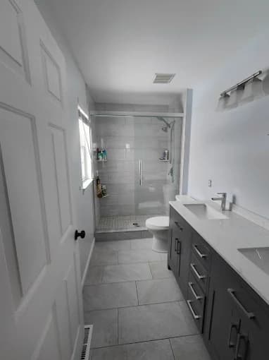 This is an image from Carrigan Painting, located in Wisconsin. The image shows a newly painted bathroom with light gray walls, a modern vanity, tiled flooring, and a glass-enclosed shower.