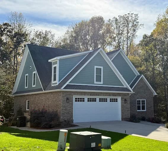 Exterior painting project by Diaz Professional Painting in Burnsville, NC. The image shows blue-gray siding, white trim, brick walls, and a white garage door.