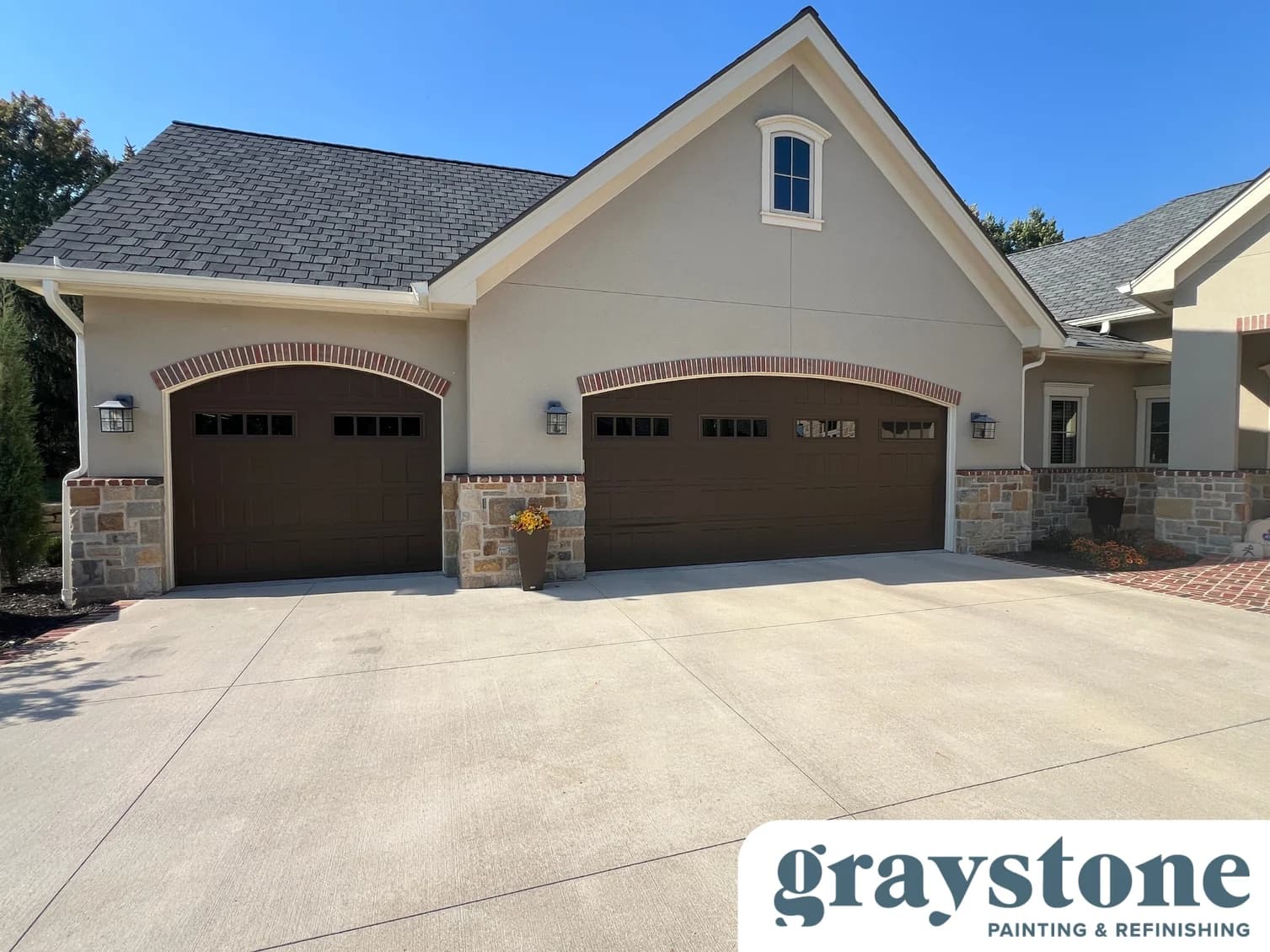 This is an image from Graystone Painting and Refinishing. The image is an exterior home in Kansas City KS with freshly painted stucco and stone siding, brown garage doors, and clean trim work.