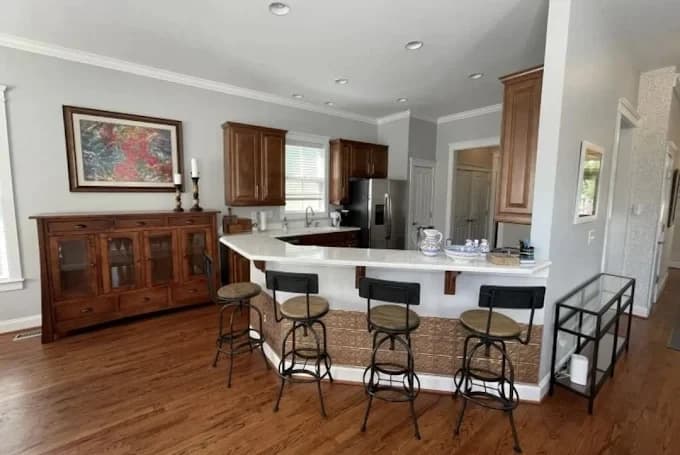 Interior painting project by Trailblaze Paints in Mooresville, NC. The image shows a kitchen and dining area with white island, wood floors, bar stools, and built-in cabinets.