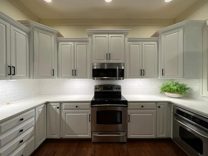 Cabinet painting project by Huskey's Paint & Design in Sylva, NC. The image shows white kitchen cabinets, a black range, tile backsplash, and dark counters.