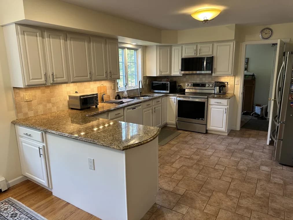 This is an image from Nyca Contractors, LLC, located in New York. The image shows a spacious kitchen with white cabinetry, granite countertops, tiled flooring, and stainless steel appliances.