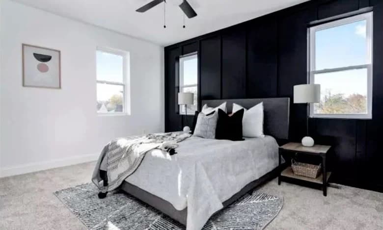 This is an image from CAZ Paintz LLC, located in New York. The bedroom features a black accent wall behind the bed, bright natural lighting, and light-colored carpet.