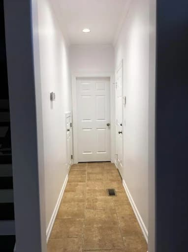 A freshly painted hallway with white walls, tan tile flooring, recessed lighting, and a closed white door at the end.