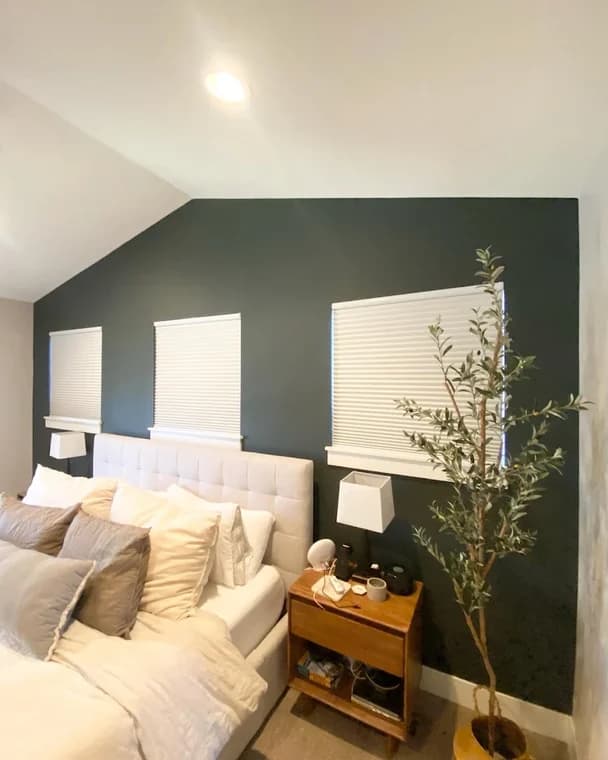 This is an image from KB Quality Painting, located in New York. The bedroom wall features a dark green accent color behind a bed with light bedding and three evenly spaced windows.