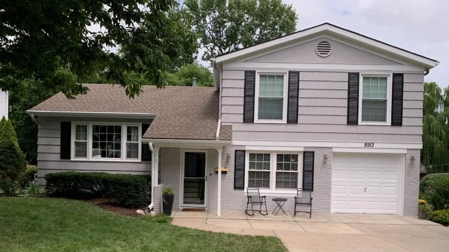 This is an image from Greg Baker Painting. The image is exterior painting in Kansas City KS showing a light gray split-level home with white trim and black shutters.