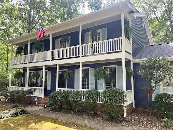 Exterior painting project by Recinos Painting in Apex, NC. The image shows a blue two-story home with white porch railings, shutters, and trim.