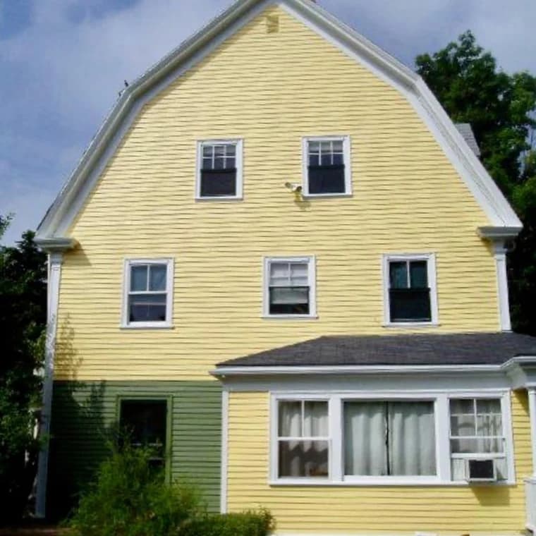 This is an image from Oliveira Painting Inc., located in Massachusetts. The photo shows a house with freshly painted yellow siding and white trim, accented by a green section on the lower left side.