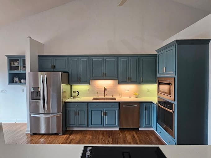 This is an image from Hearts & Hands Painting, located in Kentucky. The image shows a modern kitchen with freshly painted blue cabinets, stainless steel appliances, under-cabinet lighting, and a clean contemporary finish.