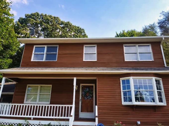 This is an image from Big Expert Painting LLC, located in New York. The photo shows a freshly painted two-story home exterior with warm brown siding, white trim, and a covered front porch.