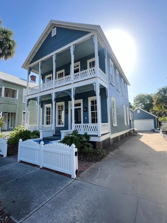 This is an image from Halls Quality Painting company, located in Fernandina Beach, FL. The image is a two-story historic-style home with fresh blue exterior paint, white trim, decorative balcony railings, and white picket fence, painted by Hall’s Quality Painting in Florida.