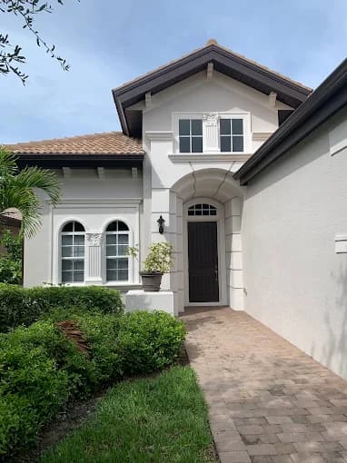 This is an image fromAncient Modern Finishes company, located in Bonita Springs, FL. The image is a freshly painted Mediterranean-style home exterior with white walls, dark trim, and arched windows by Ancient Modern Finishes