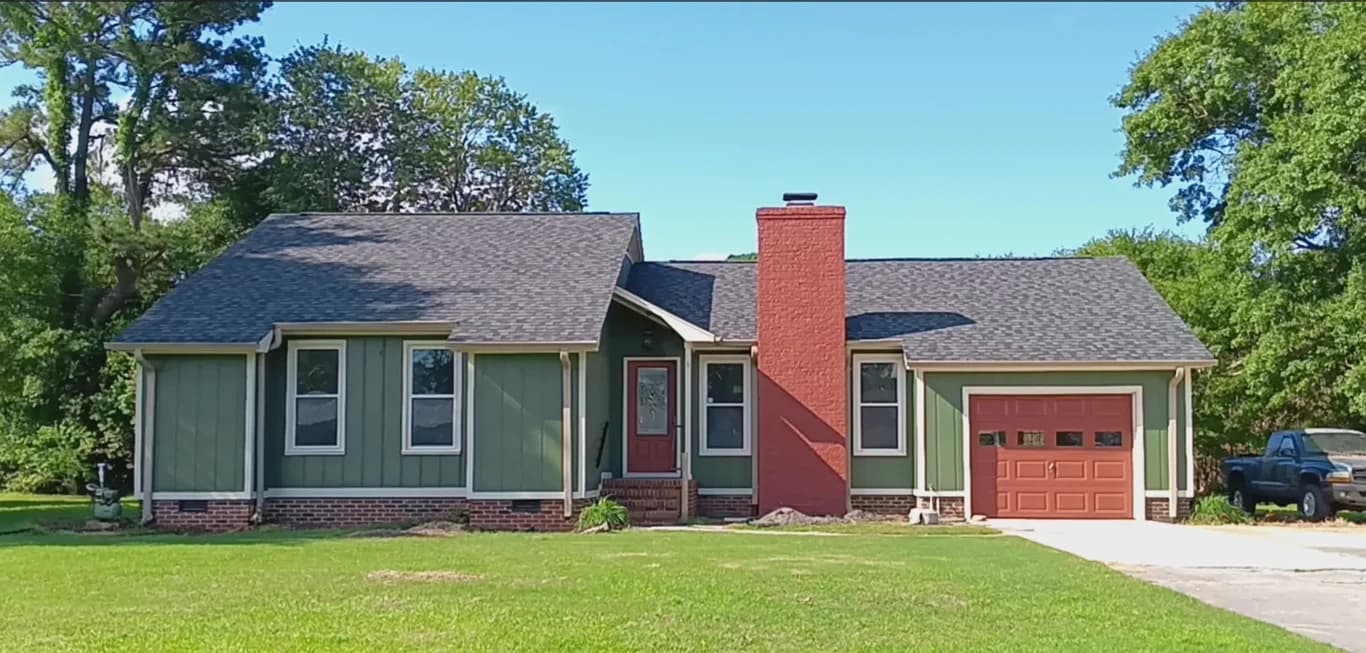 Exterior painting project by Erazo's Painting LLC in Supply, NC. The image shows a green home with red trim, a garage, and trees.