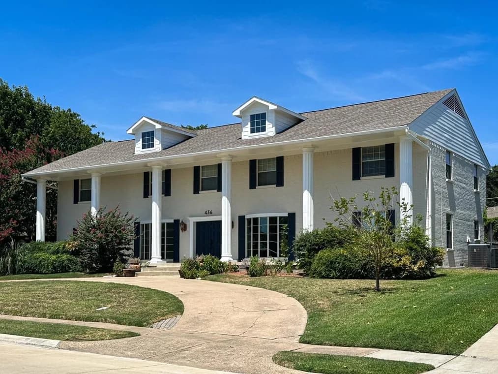 "This is an image from Highland Painting Co., located in Texas. The image displays a large two-story brick home painted in a light color with tall white columns and dark shutters."