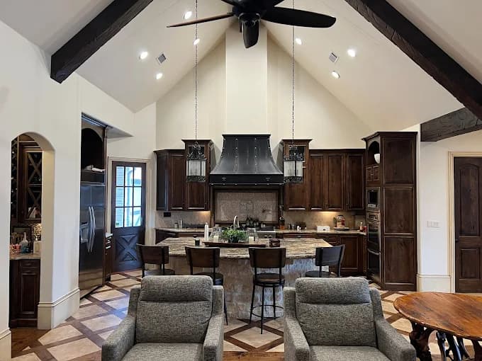 This is an image from Derheim Painting, located in Oklahoma. The photo shows a modern kitchen with high vaulted ceilings, exposed beams, dark wood cabinets, and freshly painted white walls.