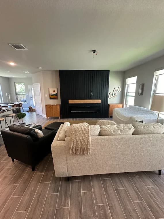 "This is an image from L&D Painting & Remodeling, located in Texas. The interior living room shows a modern black accent wall with a mounted fireplace and surrounding light-colored furnishings."