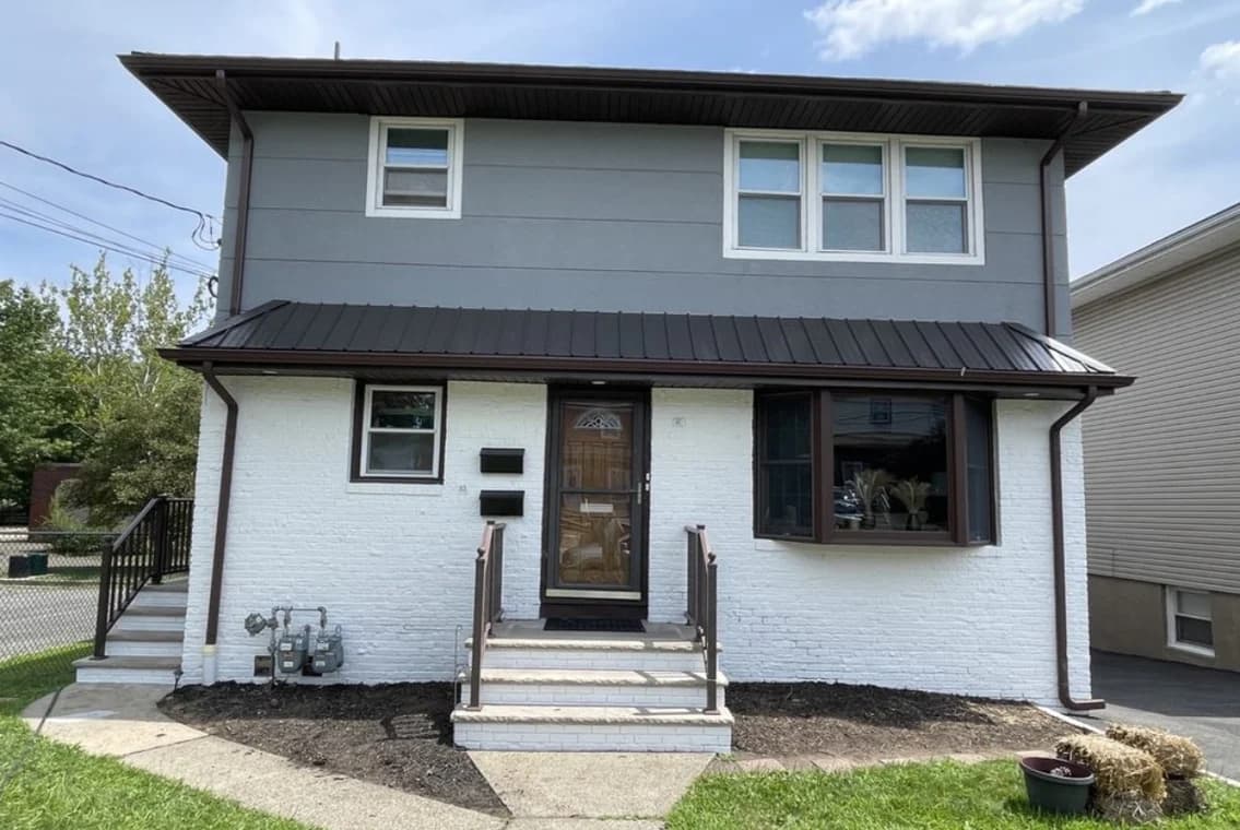 The exterior of a two-story home with white painted brick on the first level and gray siding on the second. Jordan's Painting LLC completed the transformation.