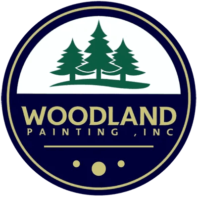 This is an image from Woodland Painting, Inc, located in Minnesota. The logo for Woodland Painting, Inc features three green pine trees inside a circular navy and gold emblem with the company name in bold lettering.