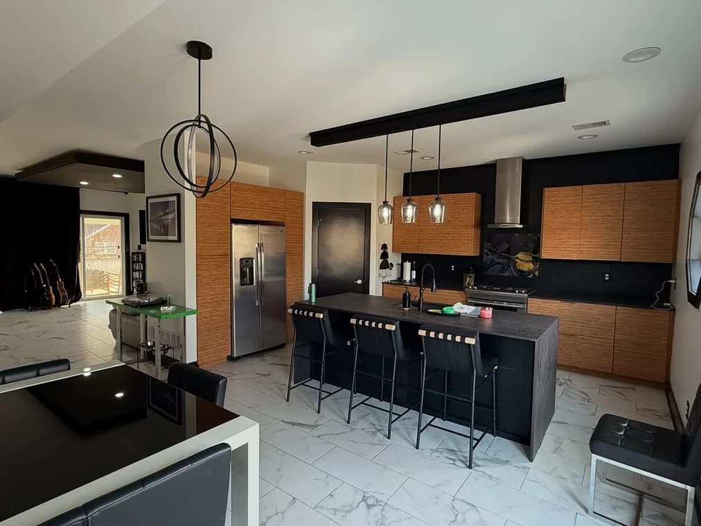 This is an image from Snap Painting Plus, located in Kentucky. The image shows a modern kitchen interior with dark accent walls, natural wood cabinetry, a large island, pendant lighting, and a clean contemporary finish.