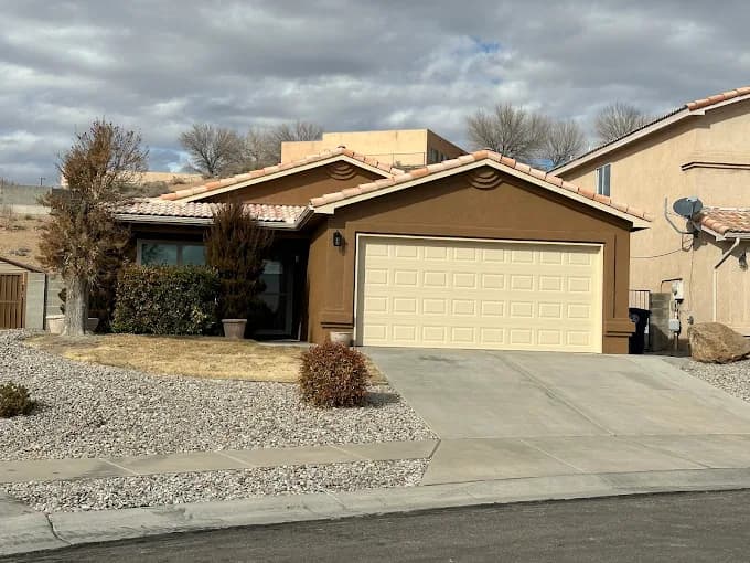 This is an image from Straight Line Painting LLC, located in New Mexico. The photo shows a single-story stucco home freshly painted in rich brown tones with a beige garage door and trim, set against a partly cloudy desert sky.