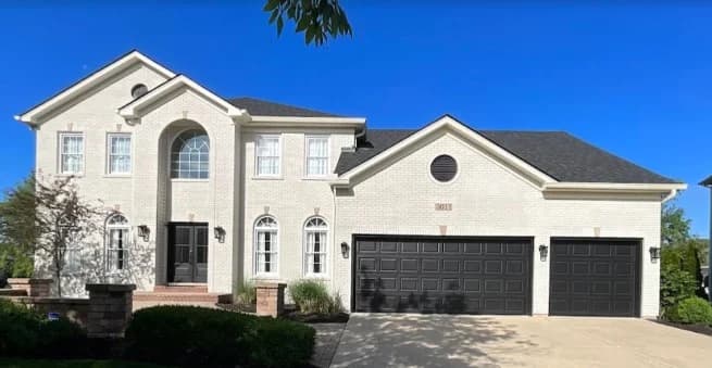This is an image from Spray-Net Chicago West, located in Illinois. The image shows an exterior two-story home with light brick, black garage doors, black front doors, white trim, and a paved driveway.