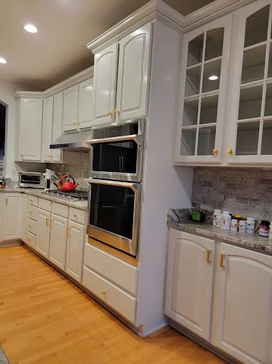 This is an image from Seven Oaks Painting Services, located in Ohio. The photo shows a modern kitchen with freshly painted white cabinets, stainless steel appliances, and light wood flooring.