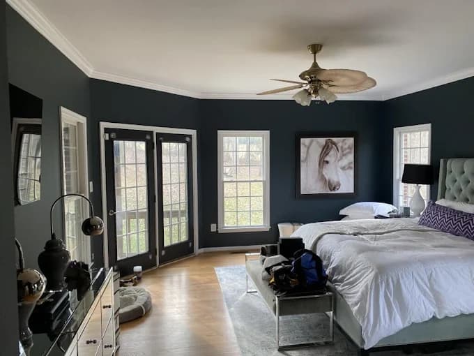 This is an image from Knight's Painting, located in New Mexico. The photo shows a freshly painted bedroom with dark gray walls, white trim, and natural light coming through large windows, featuring a neatly made bed and modern decor.
