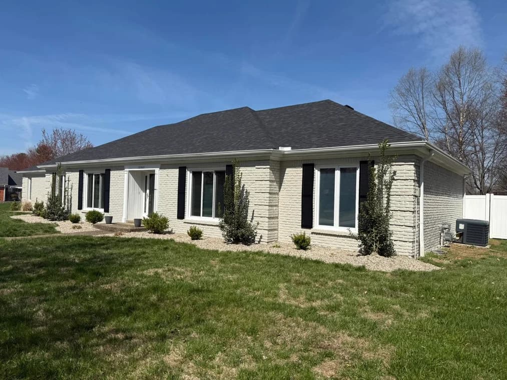 This is an image from Snap Painting Plus, located in Kentucky. The image shows a freshly painted light-colored brick home exterior with black shutters, white trim, and clean landscaping surrounding the property.