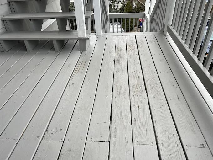 This is an image from CertaPro Painters of Boston. It displays a painted gray wooden deck with railings and stairs, showing a clean outdoor finish.