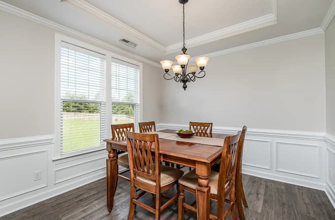 Interior painting project by Socaz Painting in Raleigh, NC. The image shows beige dining room walls, white wainscoting, crown molding, and a wood table.