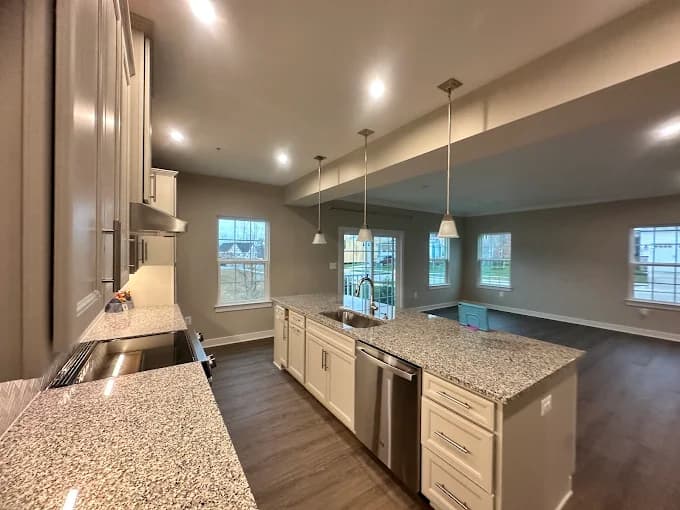 This is an image from C & V Painting Services LLC, located in Virginia. The interior photo shows a modern kitchen with granite countertops, pendant lighting, stainless steel appliances, and an open layout leading into a bright living space.