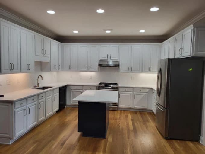 Kitchen cabinet painting project by Anthony Meggs Painting LLC in Monroe, NC. The image shows pale blue cabinets, a white island, wood floors, and recessed lights.