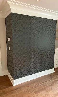This is an image from Interior Finishing NYC, located in New York. The photo shows a dark patterned accent wall with white crown molding and baseboards, set against hardwood flooring in a finished interior space.