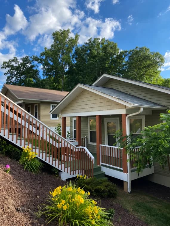 Exterior painting project by Passion Painters in Swannanoa, NC. The image shows a green home with white porch rails, red posts, and yellow flowers.