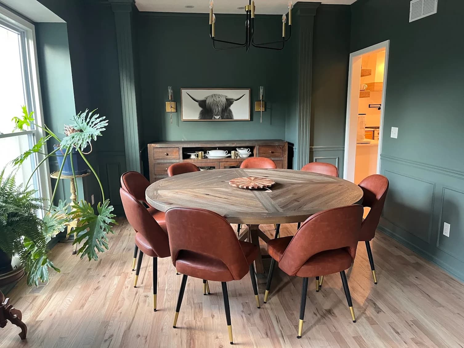 This is an image from Stack Painting. The image is an interior dining room in Kansas City KS with dark green painted walls, a round wooden table, and brown upholstered chairs.