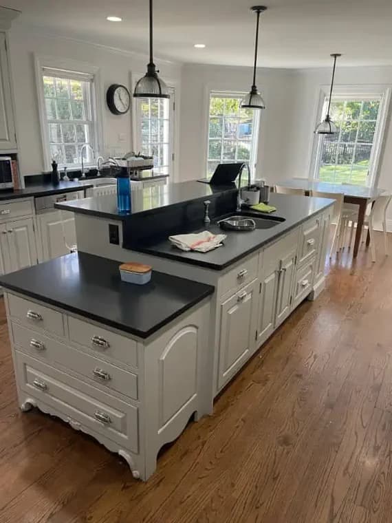 This is an image from Pier Painting Services, located in NY. The photo shows a bright kitchen with white cabinetry, black countertops, pendant lighting, and freshly painted walls.