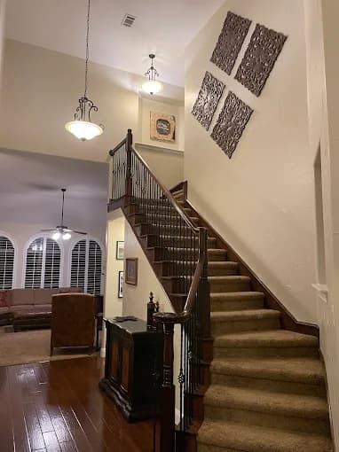 This is an image from Platinum Painting of Richardson, located in Texas. The interior staircase features freshly painted light beige walls, decorative wall panels, wood railing with iron balusters, and warm overhead lighting leading to the second floor.