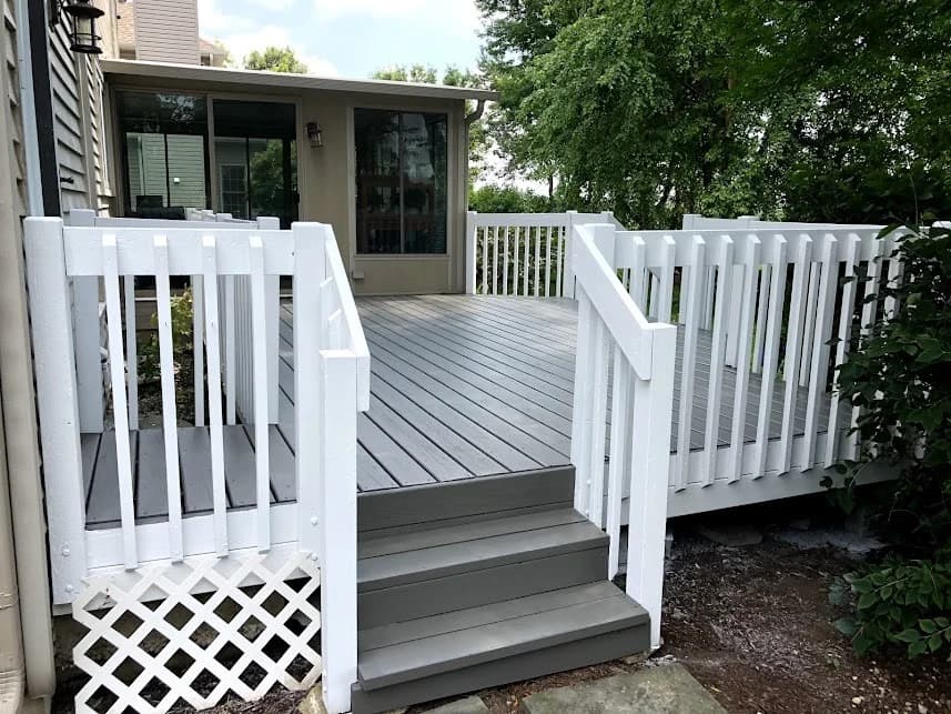 This is an image from Two Brothers Residential Maintenance & Service Corporation, located in Illinois. The photo shows a refinished backyard deck with gray floorboards, gray steps, bright white railings, and white lattice skirting