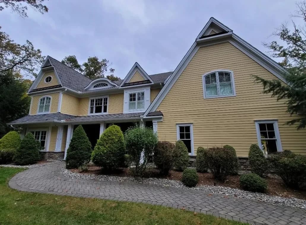 This is an image from Mark Tirondola Jr. Painting Contractor LLC in New Jersey. It highlights a yellow home with white trim and multiple roof peaks, freshly painted for a vibrant finish.