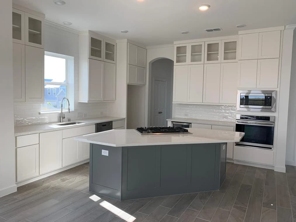 "This is an image from All Seasons Painting LLC, located in Texas. The photo shows a modern kitchen with white cabinetry, a gray island, stainless appliances, and wood-look tile flooring."