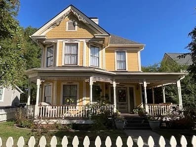 Exterior painting project by CertaPro Painters of Durham, NC in Durham, NC. The image shows a yellow Victorian home with dark trim, porch rails, and steep gables.