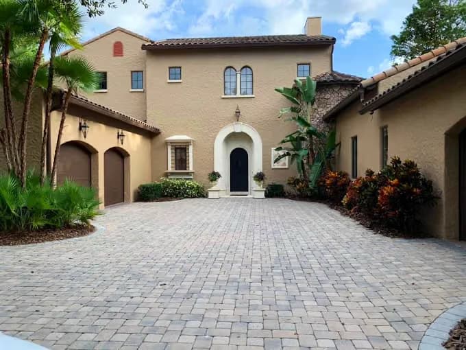 Exterior painting project by Paint Guru House Painters in Highland Park, Illinois. The image shows a tan stucco home, brown trim, tile roofs, and a paved courtyard.