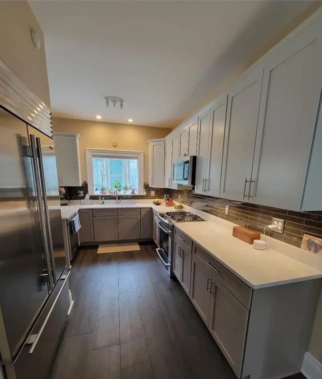 This is an image from R&R Painting & Concrete Coatings, located in New York. The modern kitchen displays white countertops, light gray cabinets, dark flooring, and stainless steel appliances.