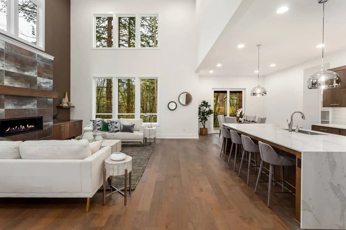 "This is an image from Roll City Painting, located in Texas. The open-concept living area features white walls, tall windows, modern furnishings, and a large kitchen island with pendant lighting."